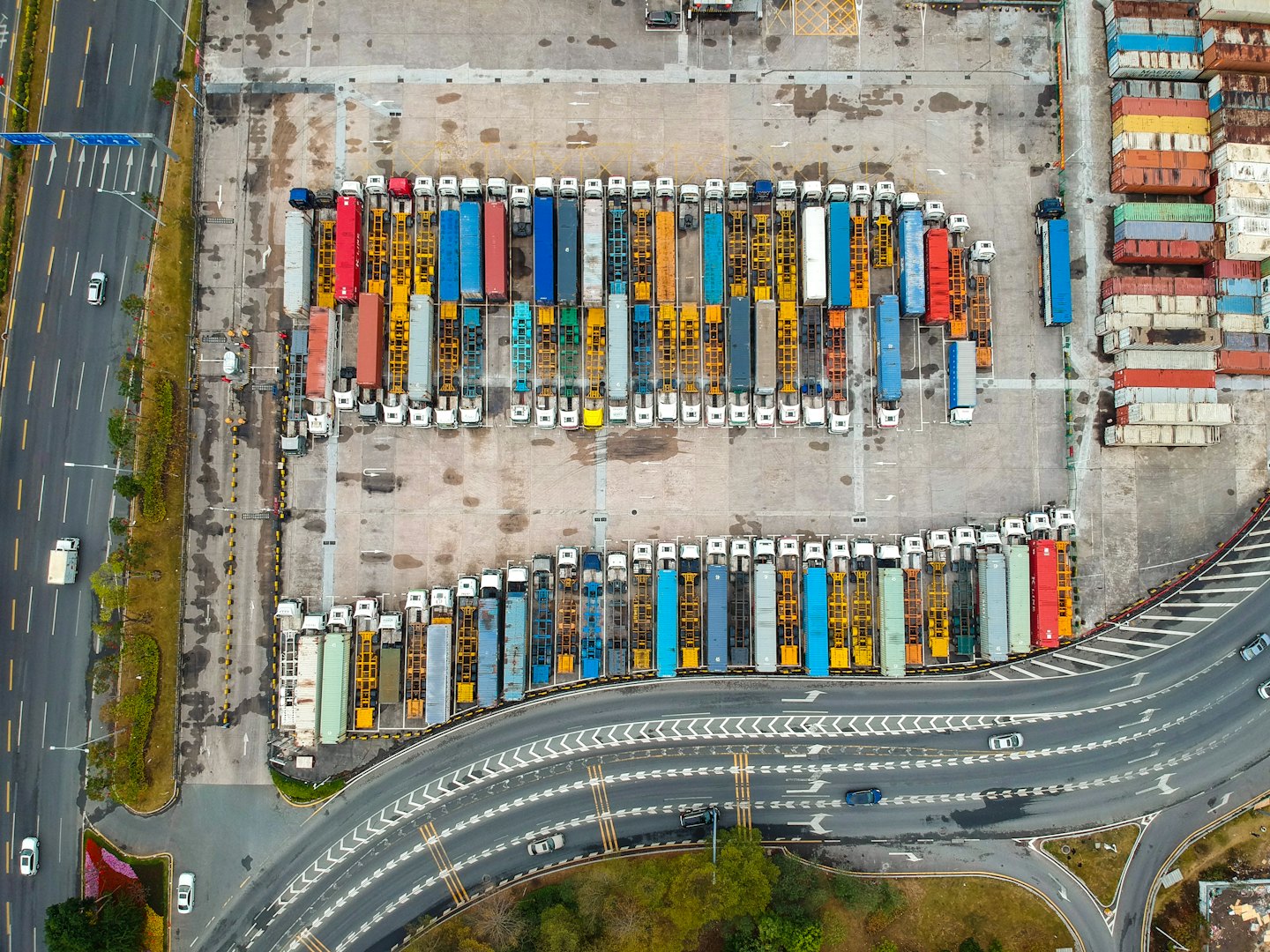 Många lastbilar och staplade fraktcontainrar fyller en stor logistikgård.