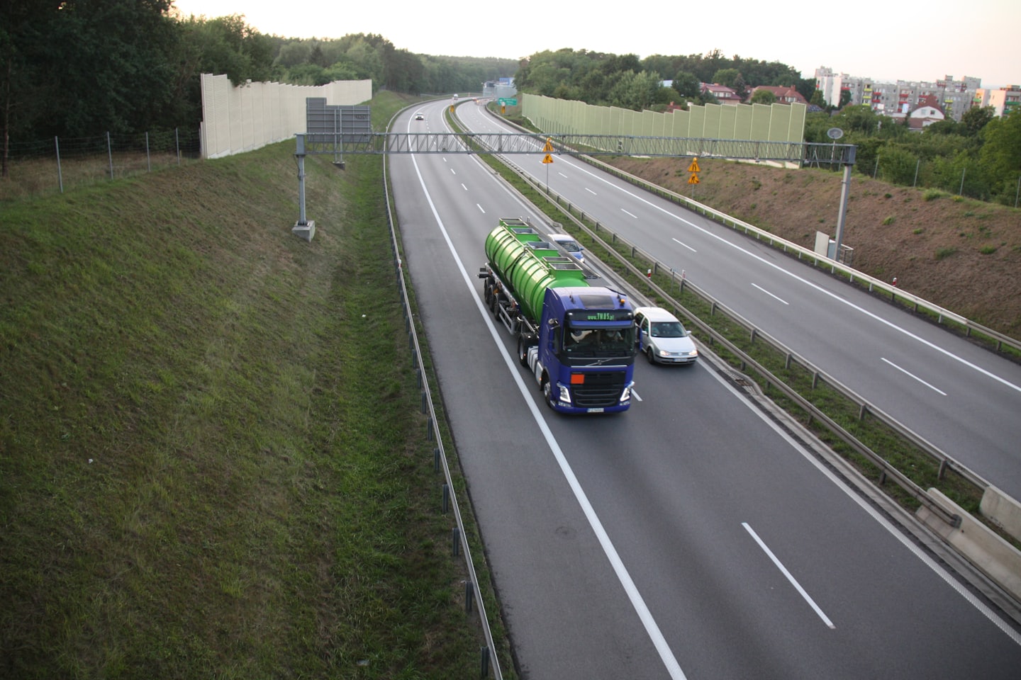 En blå lastbil med en grön tank kör på en motorväg.